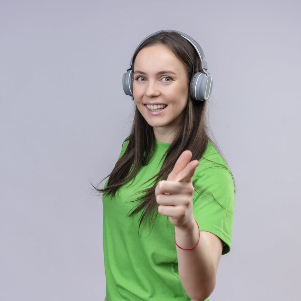 young-beautiful-girl-wearing-green-t-shirt-with-headphones-smiling-positive-happy-pointing-camera-standing-isolated-white-background-min (1)